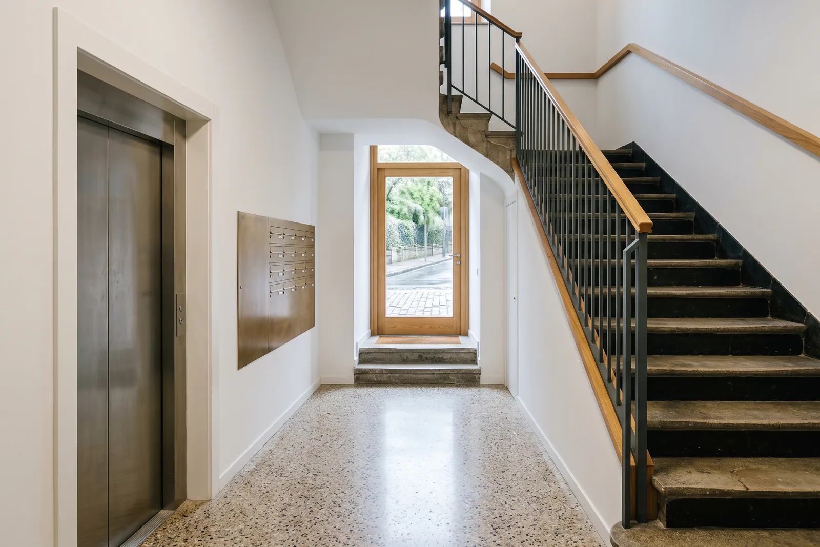Portal y escalera de una comunidad de propietarios reformados, con suelo de terrazo y barandilla nueva